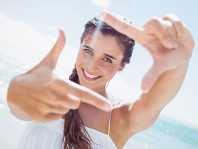 A young woman with a radiant smile is taking a selfie, capturing her joyful moment at the beach.