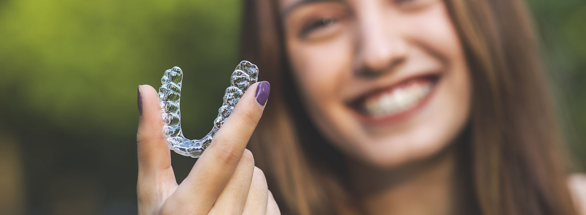 A person is holding a clear, plastic dental retainer in their hand.